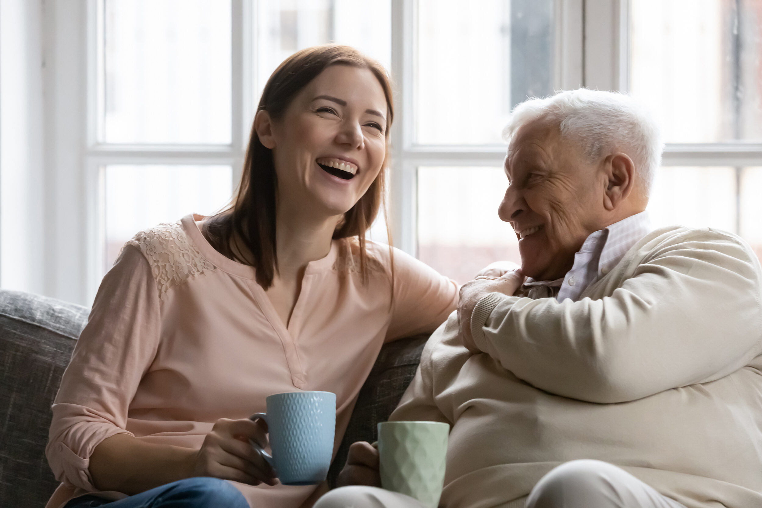 Attentive young lady caregiver visiting supporting glad elderly man patient