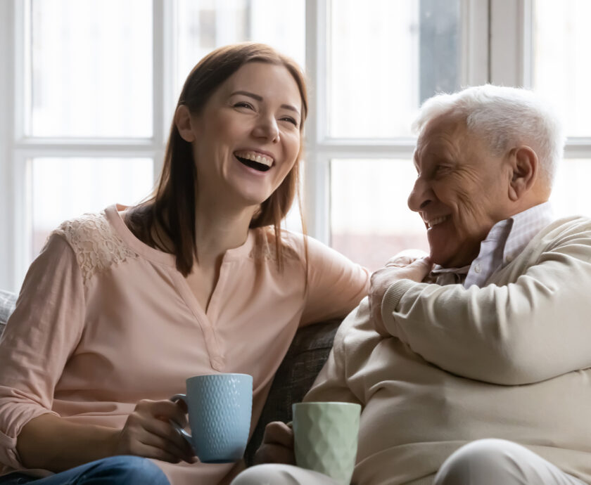 Attentive young lady caregiver visiting supporting glad elderly man patient