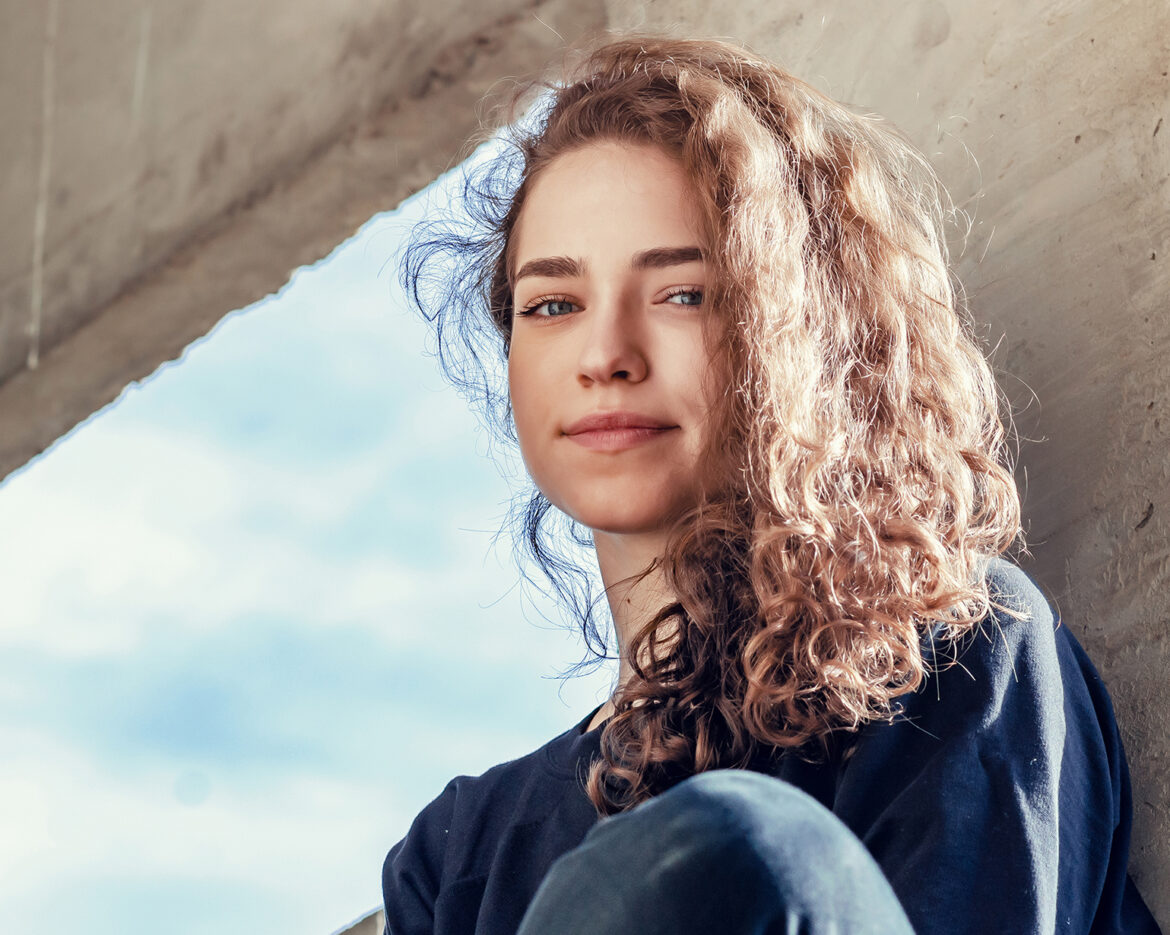 Lovely girl in dark clothes sits on concrete block in industrial