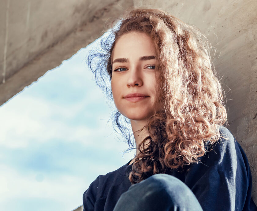 Lovely girl in dark clothes sits on concrete block in industrial